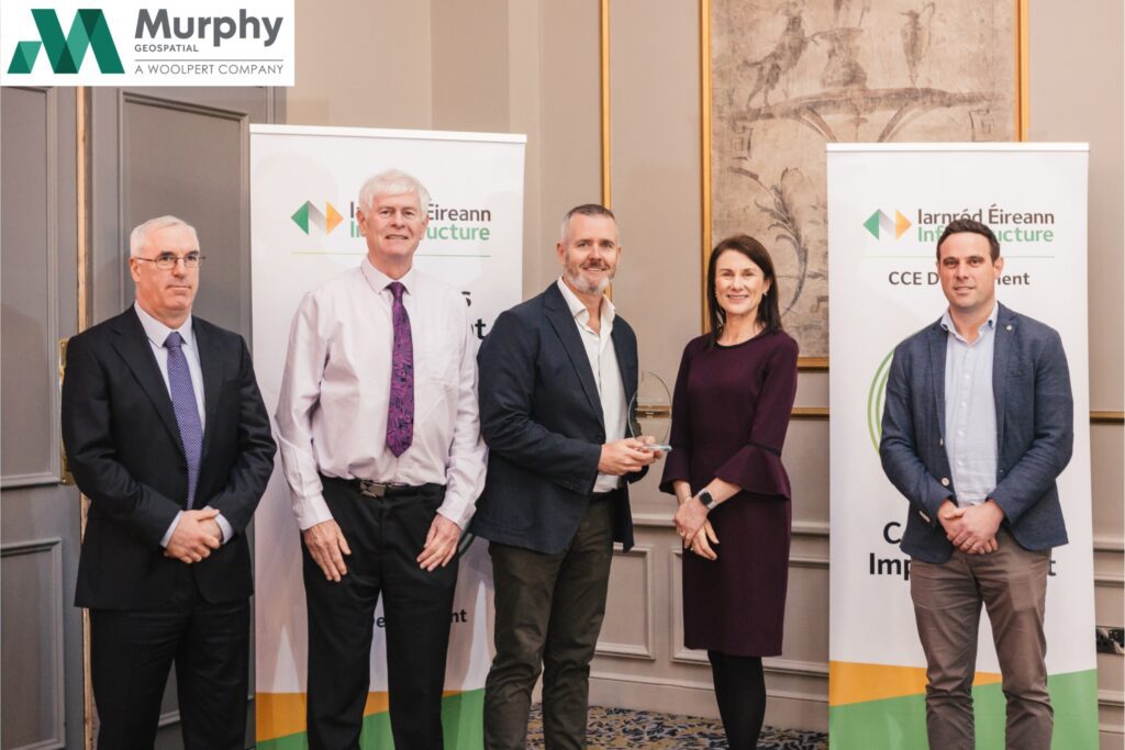 Group of five people standing indoors during an award presentation event, with Murphy Geospatial branding banners behind them.
