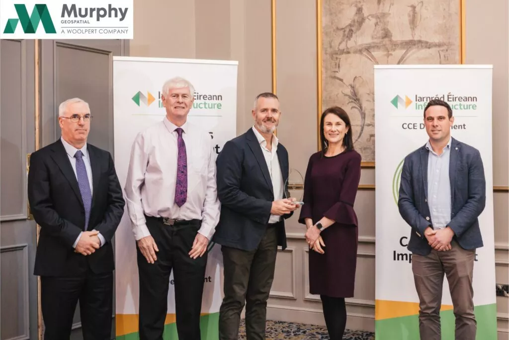 Group of five people standing indoors during an award presentation event, with Murphy Geospatial branding banners behind them.